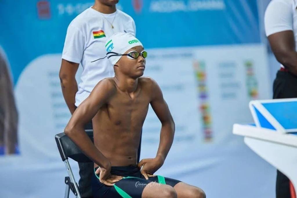 A young male swimmer sitting on a chair, wearing a swim cap and goggles, preparing for a competition.